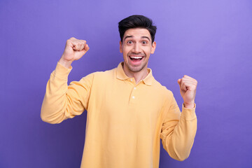 Photo of lucky excited guy wear yellow polo screaming yeah rising fists isolated violet color...