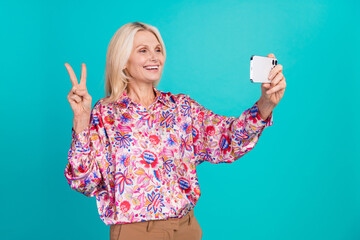 Photo of shiny cute woman dressed print shirt tacking selfie modern device showing v-sign isolated turquoise color background