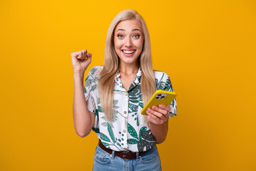 Photo of satisfied woman with straight hair dressed shirt hold smartphone clenching fist win bet...