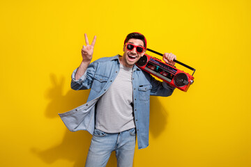 Photo of excited funky man dressed jeans shirt dark spectacles showing v-sign listening boom box...