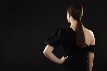 Woman in elegant dress on black background, back view. Space for text