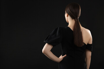 Naklejka premium Woman in elegant dress on black background, back view. Space for text