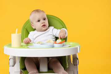 Cute little baby with healthy food in high chair on orange background, space for text