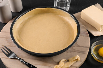 Pie tin with fresh dough and ingredients on black table. Making quiche
