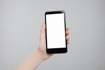 Woman holding smartphone with blank screen on grey background, closeup. Mockup for design