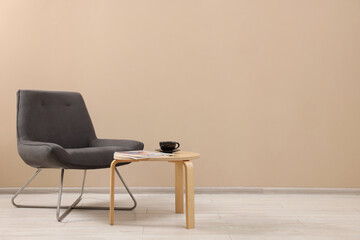 Comfortable armchair and coffee table near beige wall indoors, space for text. Interior design