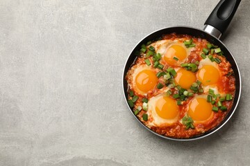 Delicious Shakshuka in frying pan on light grey table, top view. Space for text