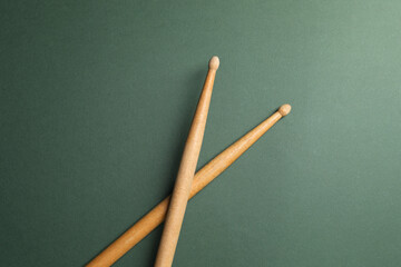 Two wooden drum sticks on olive background, top view