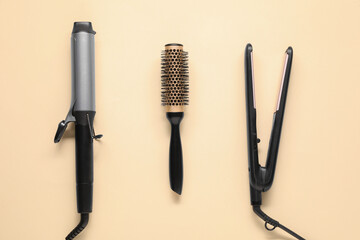 Curling iron, hair straightener and round brush on beige background, flat lay