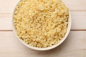 Delicious bulgur in bowl on wooden table, top view