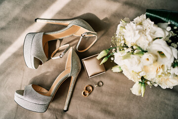 Wedding rings lie next to a bouquet of flowers and the bride high-heeled shoes