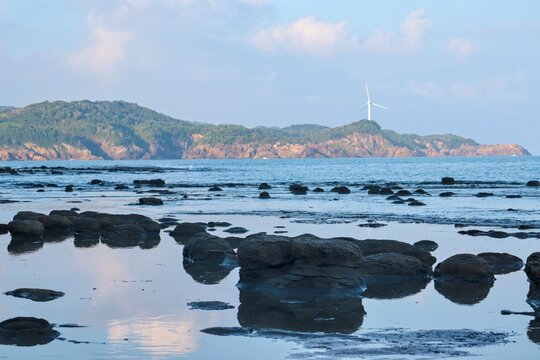 Rocky tidal shoreline with a green headland across the sea