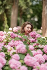 Naklejka premium Hydrangeas Happy woman in pink dress amid hydrangeas. Large pink hydrangea caps surround woman. Sunny outdoor setting. Showcasing happy woman amid hydrangea bloom.