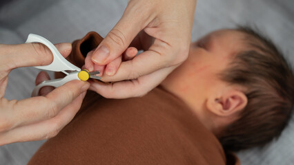 Mom cuts her newborn son's fingernails with small children's scissors.