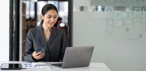 Asian businesswoman using mobile phone and working on laptop at office.