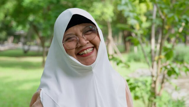 Closeup face of cheerful elderly woman covered with headscarf smiling outdoors. Casual Islamic girl in park. Freedom and relaxing outdoors. Happiness, smile, and face of Islamic female person with joy