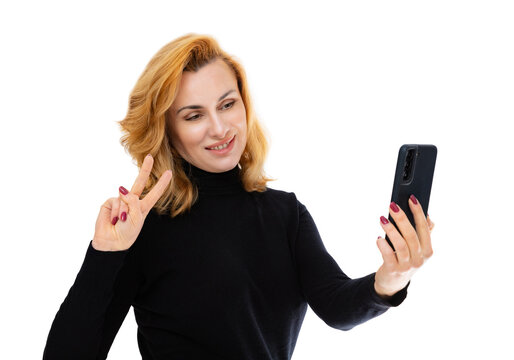Portrait of forty year old woman  take selfie and make v-signs, isolated on white background. Woman in black turtleneck smiling and posing in studio.