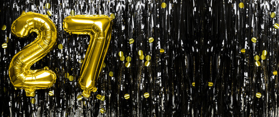 Gold foil balloon number number 27 on a background of black tinsel decoration. Birthday greeting...