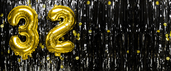 Gold foil balloon number number 32 on a background of black tinsel decoration. Birthday greeting...