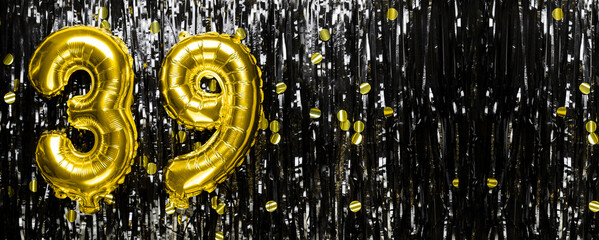 Gold foil balloon number number 39 on a background of black tinsel decoration. Birthday greeting...