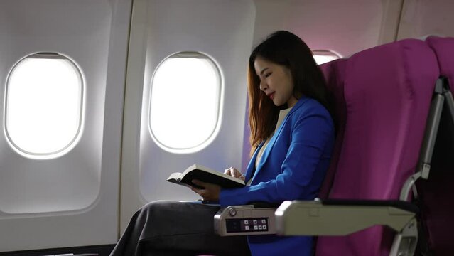 Happy Asian businesswoman reading a book while traveling on an airplane.
