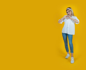 Full body blonde girl holding hands over chest in heart shape gesture. Standing over isolated...