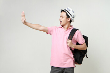 Asian man backpacker showing his palm hand. giving stop gesture. digital nomad and travelling concept. on isolated background
