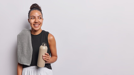 Smiling Latin sporty woman wearing sportswear holds sport bottle with water feels thirsty after...