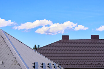 Brown gray silver metal tile profile on the roof of a house and blue clear sky