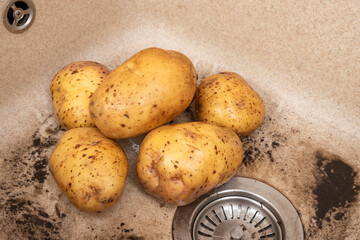 Washing potatoes for lunch in a modern kitchen sink. Water rinsing potatoes in sink.