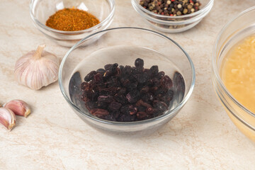 Soaking raisin before cooking in modern multi cooker pilaf in bowls on a kitchen table near other prepared ingredients. Cooking pilau with meat in multicooker.