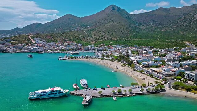 Elounda Fishing Town Port with vessels and boats on a sunny day with a calm sea. Greek Paralia Schisma Elountas Compact Beach. Calm waters pedal boat umbrella rentals by Mediterranean Sea