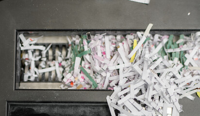 Postrzępione dokumenty firmowe wypadające z ostrza niszczarki do papieru