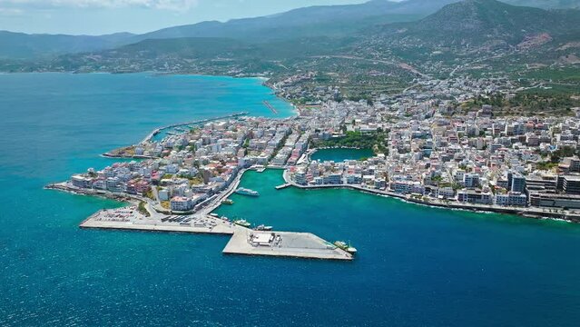 Aerial panoramic view of Agios Nikolaos City on Crete Island in Greece in 4K. Sunny summer City day on Mediterranean Island with turquoise water. Paralia Kitroplatia, Ammos, Yachting Sailing Cruises