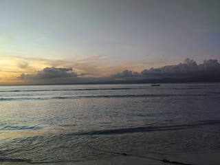 Serene sunset over calm ocean waves, a distant boat silhouetted against the fading light.