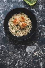 Bowl with brown rice and seared scallops on a dark-brown granite background, vertical shot with space, top view