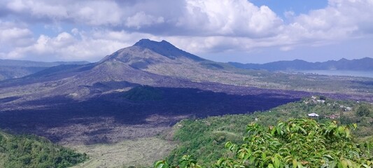Panoramic view of a majestic volcano dominating a lush, green landscape under a cloudy sky.