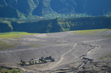 High-angle view of a volcanic crater landscape, showing a dusty plain with a small group of people...
