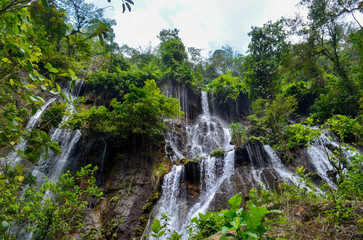 Fototapeta premium Lush green foliage frames a cascading waterfall tumbling down a rocky cliff face.