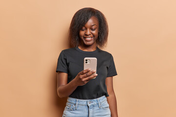 Smiling dark skinned woman using smartphone app chatting or ordering holding mobile phone reads...