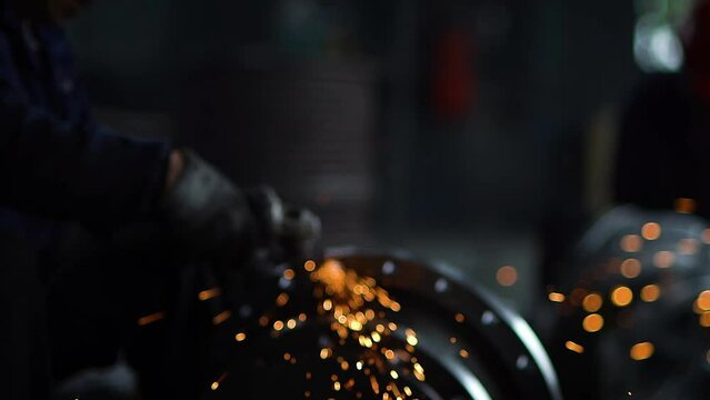 Close-up of sparks from grinding metal structures at a factory in China, factory worker grinds metal, bright golden sparks comes out