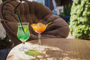 two glasses of cocktails stand on a table on the summer terrace of a cafe. Mojito and Aperol spritz...