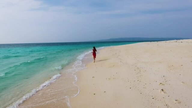 Aerial view of a girl in a red dress running along the coastline of a tropical sandy beach on an island on a sunny day, tropical beach in the philippines