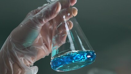 A scientist's hand shakes a flask with a blue liquid in a medicinal chemistry laboratory - Powered by Adobe