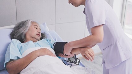 young nurse measures the blood pressure of elderly woman patient on hospital bed