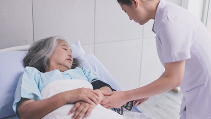 young nurse measures the blood pressure of elderly woman patient on hospital bed