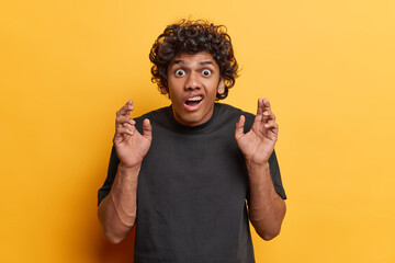 Studio shot of young scared Hindu male student wearing casual black tshirt standing isolated in...