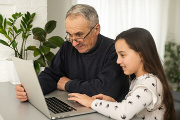 Fototapeta premium Portrait of grandfather and granddaughter doing homework with laptop.