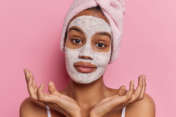 Beauty and cosmetology concept. Studio close up of young pretty European woman expressing hesitation applying natural clay face mask as skin care procedures spreading palms sideways on pink background - obrazy, fototapety, plakaty