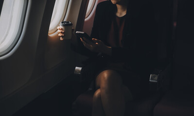 Blonde female tourist checking incoming notification on smartphone sitting on seat of airplane with netbook.Young businesswoman share media from telephone on laptop computer during plane flight